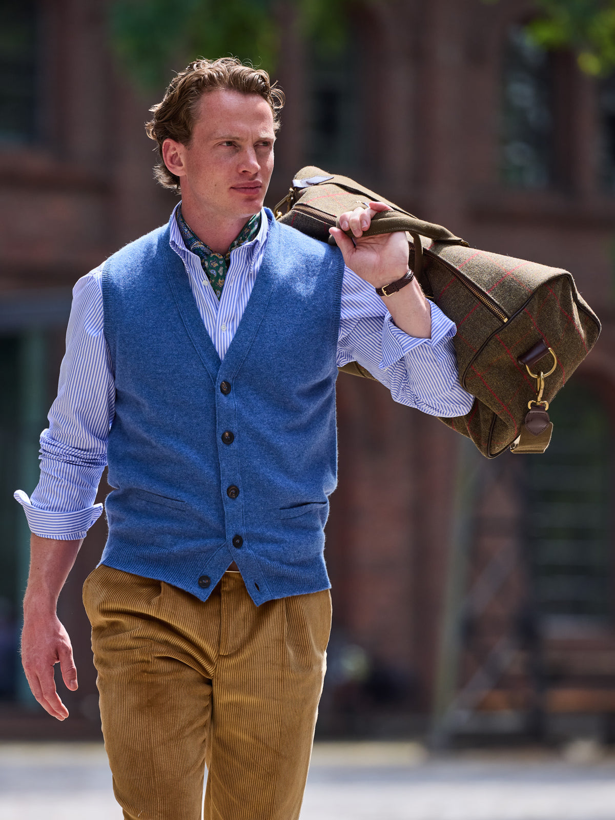 Weekender aus Lovat Tweed in Olive an den Griffen über die Schulter gehängt, zu blauer Strickweste – John Crocket